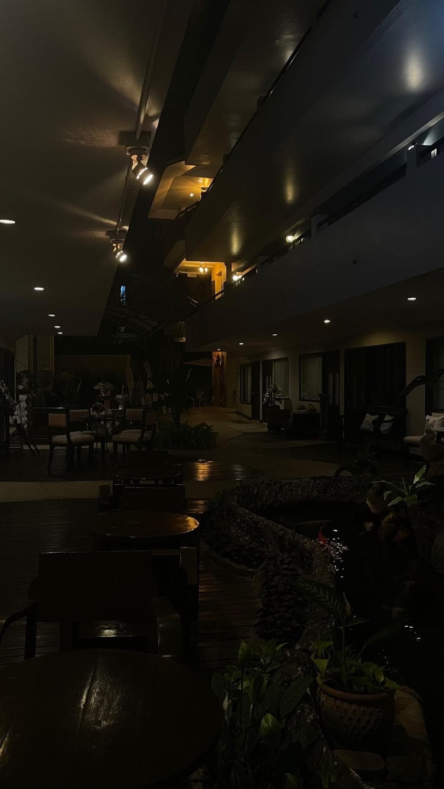A dimly lit open-air resort walkway at night, warm downlights over tables and a koi pond.