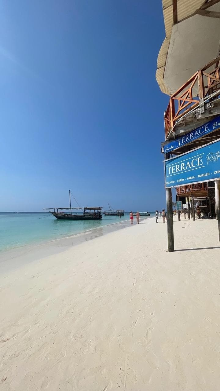 A wooden dhow moored off the white sand at Nungwi beach under a clear blue sky.