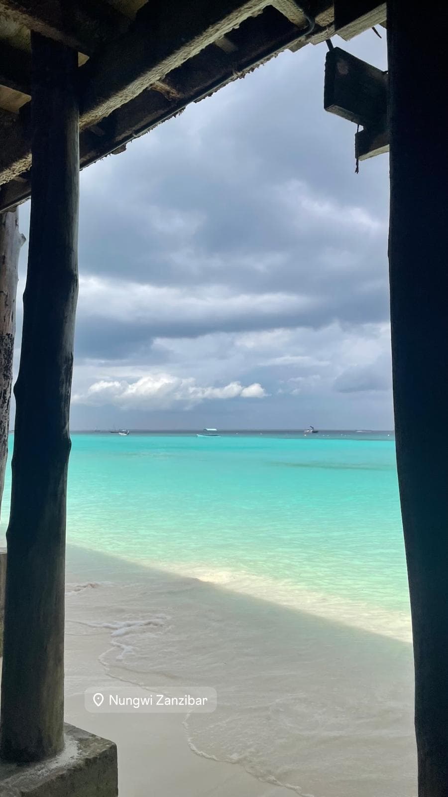 Turquoise shallows seen between the timber posts of a jetty at Nungwi, storm cloud gathering offshore.