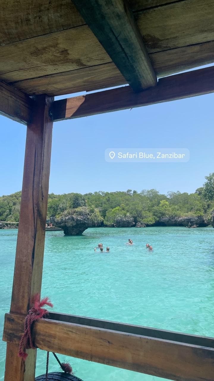 Swimmers in a clear turquoise lagoon, seen from beneath the timber canopy of a moored boat.